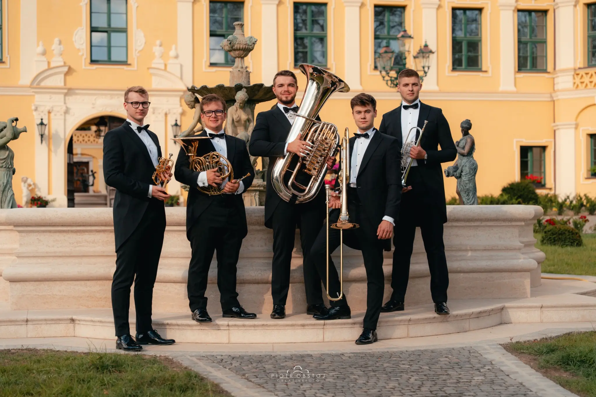 Pięciu muzyków Silver Brass z trąbkami, waltornią, puzonem i tubą przed pałacem